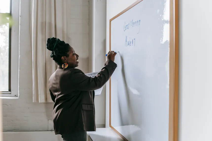 Side view of smiling African American woman writing on whiteboard standing in modern school classroom