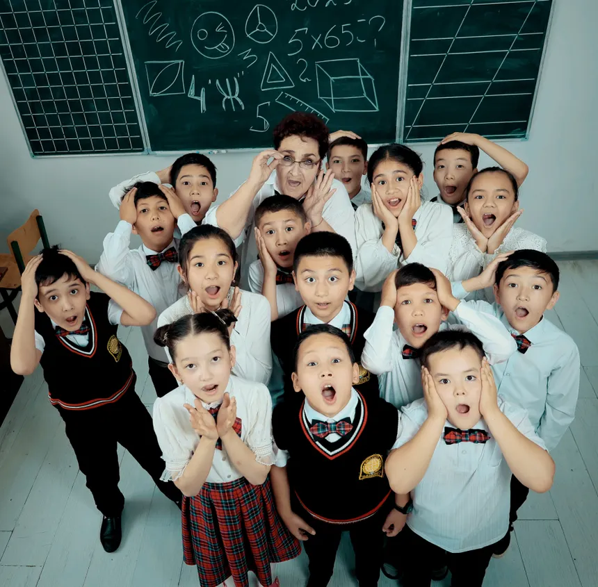 A group of school children in uniforms posing with their teacher inside a classroom.