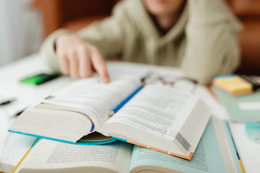 A person pointing at an open book on a desk, focusing on learning.