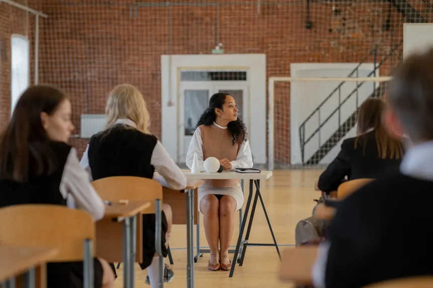 Teacher sitting at desk during class in a school gymnasium.
