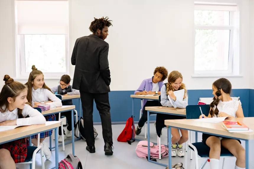 A teacher watches over students who are engaged in classroom activities on a bright day.