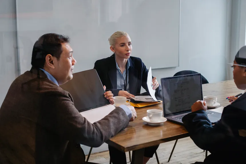 Multiracial colleagues in formal clothes sitting at table with laptop and documents while discussing details of business plan