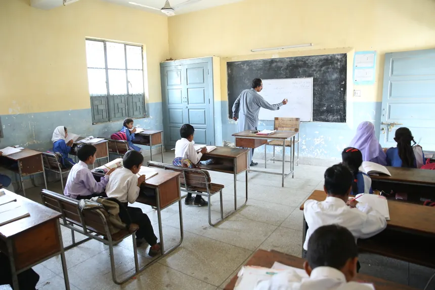 Elementary classroom with attentive students and teacher at blackboard, promoting education.